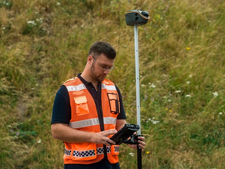 Surveyor using a CHC Navigation GNSS RTK rover on a survey pole to collect field positioning data in open terrain
