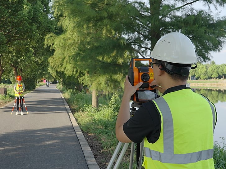 Two surveyors conducting a total station traverse along a road, with the instrument operator sighting a prism pole target