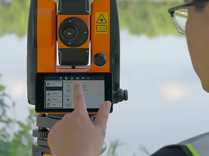 Two surveyors conducting a total station traverse along a road, with the instrument operator sighting a prism pole target